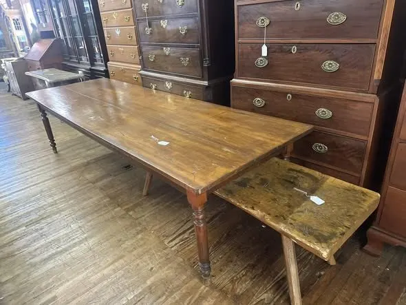 Long harvest table with a worn wooden bench, chest of drawers behind