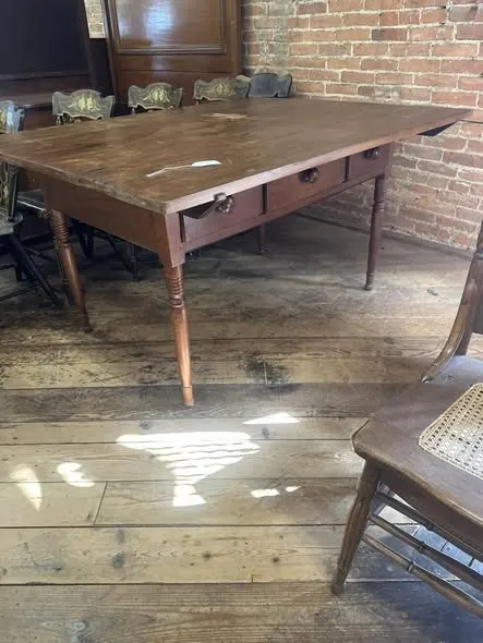 Farm table with three drawers in front of a brick wall